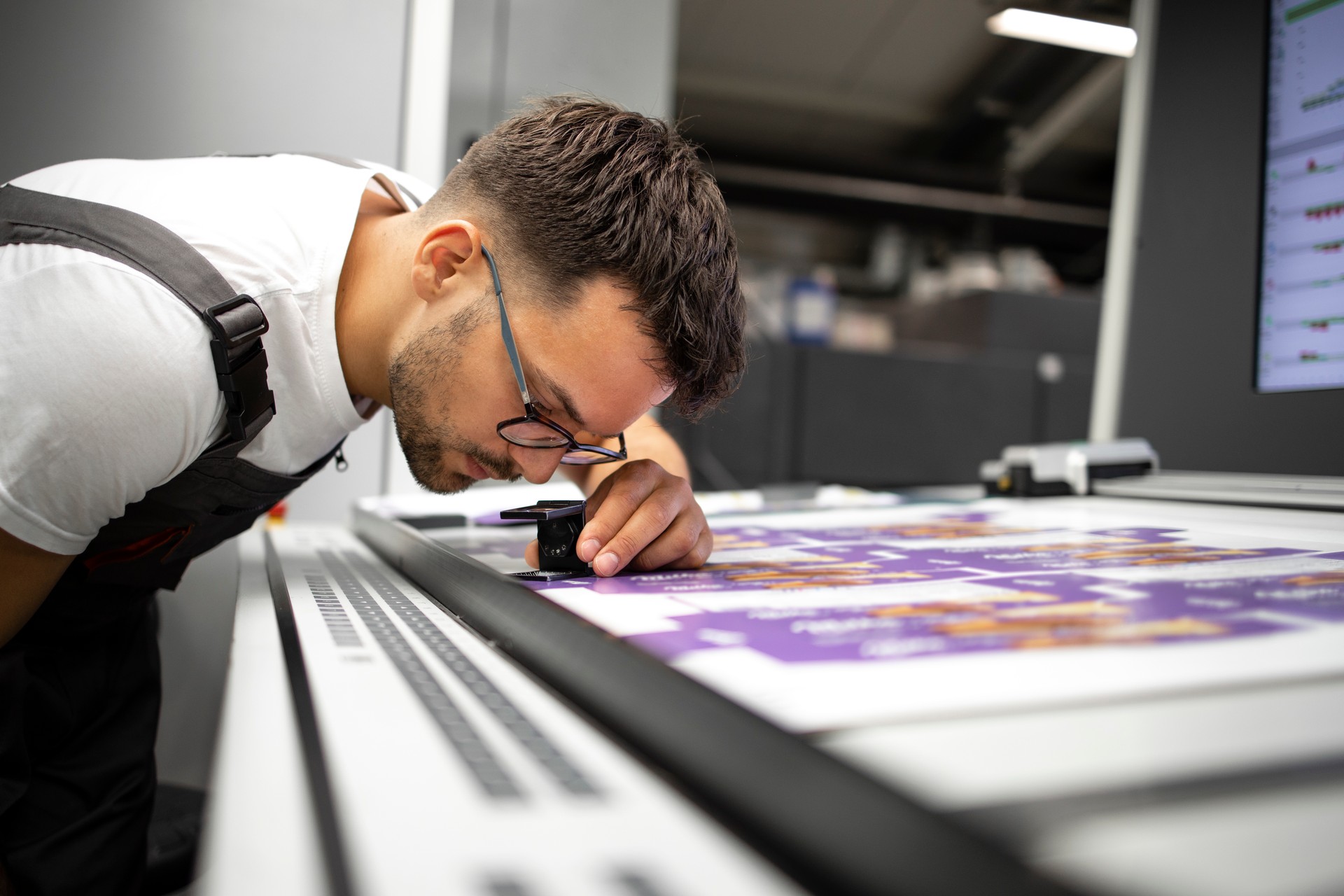 Trabajador comprobando la calidad de impresión de gráficos en imprenta moderna.